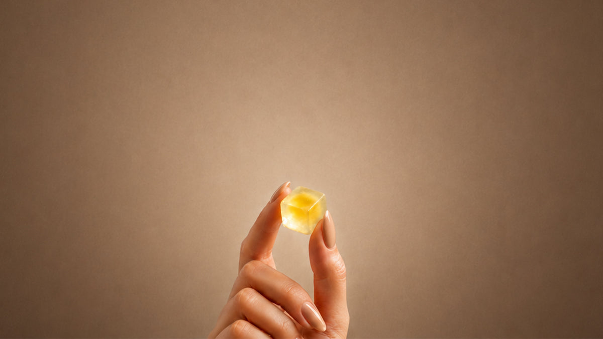 A hand holding a single golden gummy